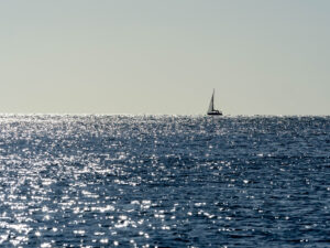 Distant sailboat crosses the horizon against a sparkling blue sea